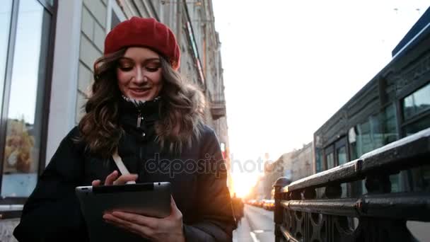 Junges attraktives Mädchen mit Tablet im Sonnenuntergang in der Stadt. Lifestyle-Porträt einer jungen Frau, die ein Smartphone-Tablet für soziale Netzwerke nutzt — Stockvideo