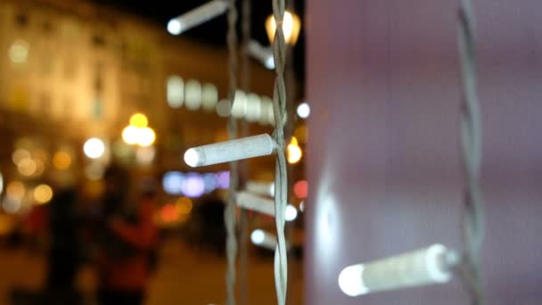 Guirnaldas brillantes que se balancean en el viento en el fondo de la ciudad de noche borrosa con coches en movimiento y multitudes de personas, spaseski hacer compras para la Navidad — Vídeo de stock