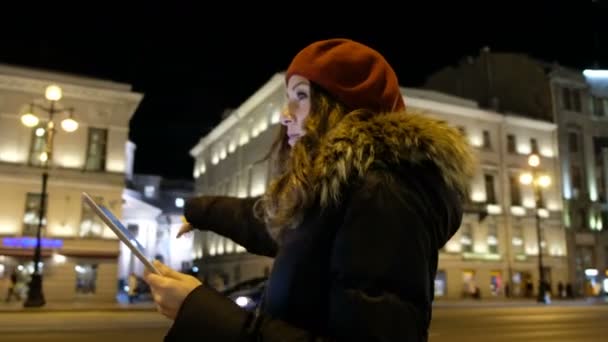 Menina atraente olha para fora do tablet e esperando o ônibus à noite na cidade . — Vídeo de Stock