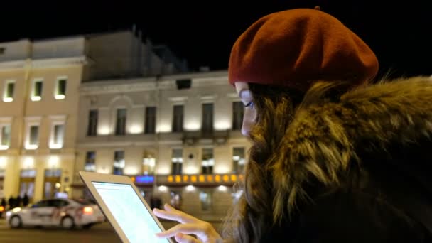 Attractive girl looks out the tablet and waiting for the bus in the evening in the city. — Stock Video