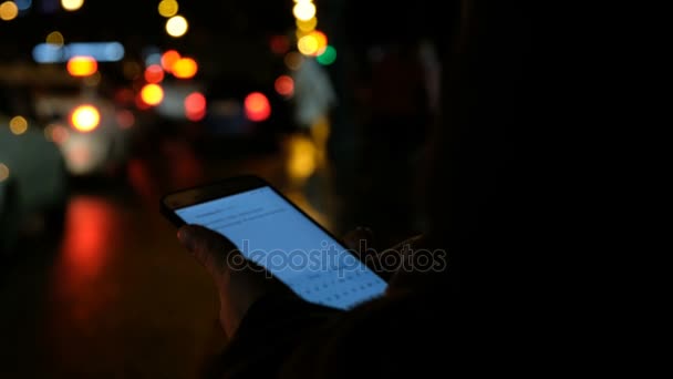 女孩指着屏幕上的智能手机背景照明散的颜色光在夜间城市, 时髦使用手和短信手机 — 图库视频影像