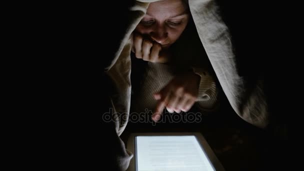 Menina sob um cobertor olhando para a tela do tablet e vira as páginas com os dedos, close-up — Vídeo de Stock