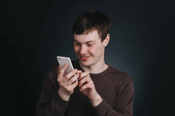 Мужчина смотрит на экран мобильного телефона и набирает сообщение, портрет человека крупным планом в студии на темном фоне — стоковое фото