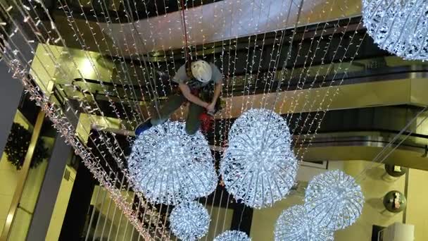 Промышленный альпинист устанавливает рождественские украшения в неподдерживаемом пространстве в торговом центре — стоковое видео