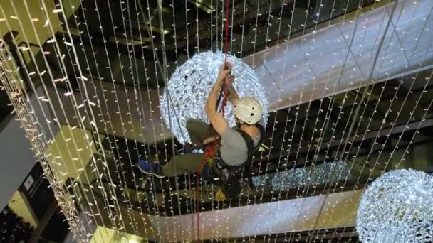 L'arrampicatore industriale monta decorazioni natalizie nello spazio non supportato del centro commerciale — Video Stock