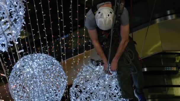 Industrial climber mounts Christmas decorations in the unsupported space in the shopping center — Stock Video