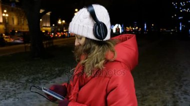 Çekici kız kış akşamları bir akıllı telefon kulaklık müzik dinleme.