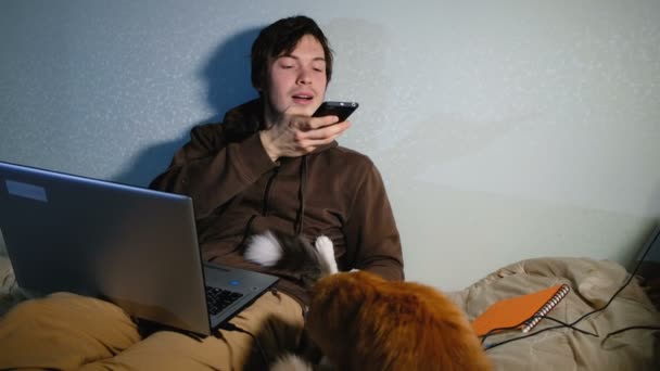 Jonge man nemen van foto's op smartphone mijn katten zittend op mijn bed met mijn laptop, katten spelen en afleiden van het werk. — Stockvideo