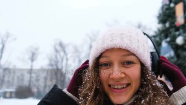 Kaukasische meisje vangsten sneeuwvlokken met zijn mond in een Park met koptelefoon closeup. — Stockvideo