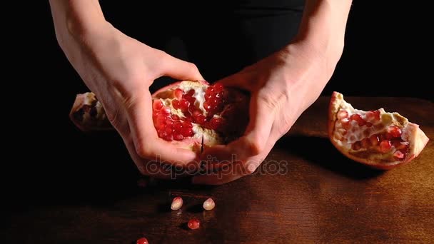 Female hands break the half a ripe pomegranate in half on a brown Desk and dark background, close-up slow motion in 4K. — Stock Video