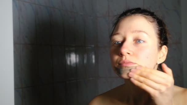 Chica joven obtiene una máscara cosmética de arcilla azul en el baño, 4K . — Vídeos de Stock