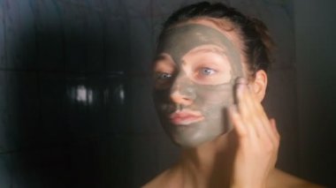 Güzel genç kadın banyoda, 4 k mavi kil kozmetik maskesi uygulama.