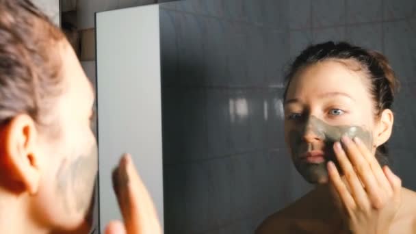 Giovane ragazza che applica una maschera cosmetica di argilla blu in bagno, 4K . — Video Stock