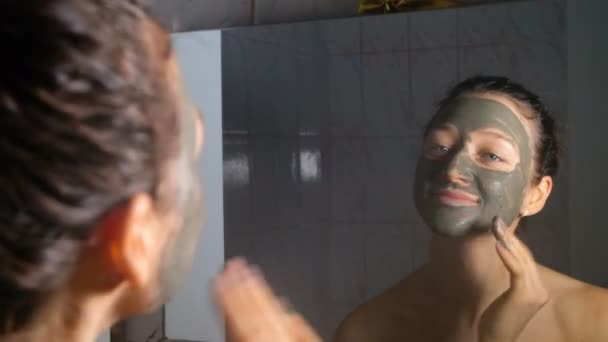 Joven chica caucásica aplicando máscara cosmética de arcilla azul en el baño, 4K . — Vídeo de stock