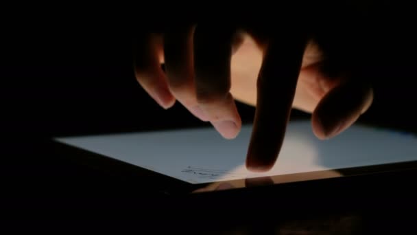 Main dessine des mots avec un doigt sur la tablette dans l'obscurité gros plan, 4k . — Video