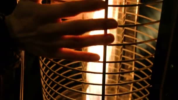 Un hombre está calentando sus manos cerca de una chimenea artesanal o una lámpara de queroseno al aire libre, 4K . — Vídeos de Stock