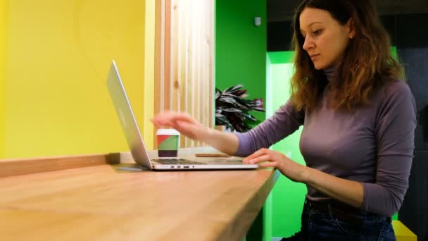 Caucásico chica en los cafés abre un portátil y bebe café, un freelancer trabaja en un café, 4k . — Vídeos de Stock