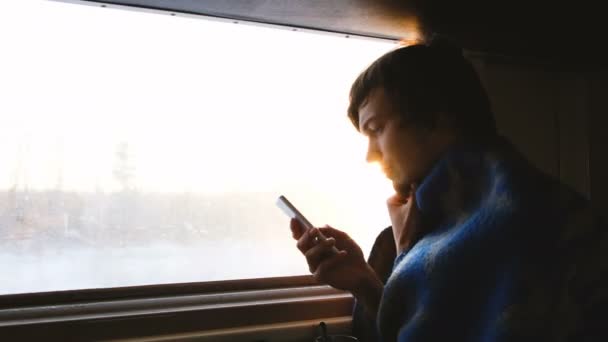 Hombre en un cuadros viajando en un tren y usando el teléfono inteligente al atardecer, 4k . — Vídeo de stock