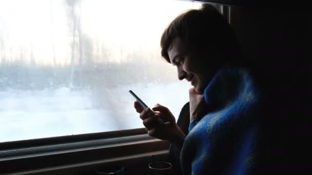 Homme heureux en plaid voyageant dans un train et utilisant le smartphone au coucher du soleil, 4k . — Video