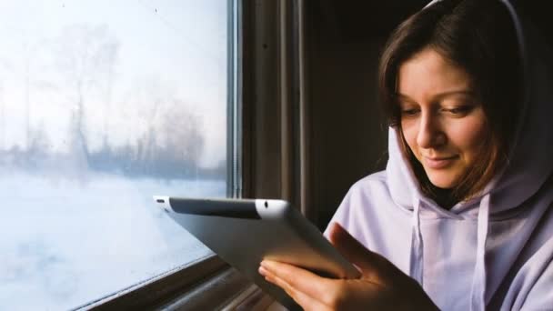 Güzel beyaz kız trende bir tablet sahiptir ve günbatımı, 4 k, pencereden görünüyor. — Stok video