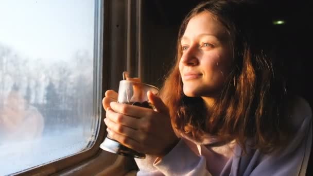 Hermosa chica caucásica bebe té y mira por la ventana en el tren y sonríe, 4k . — Vídeos de Stock