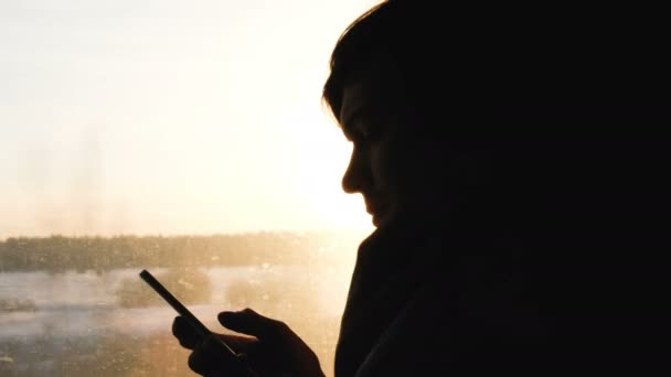 Silhueta de um homem em xadrez, um homem está viajando em um trem e usando um smartphone em um fundo de pôr do sol, 4k . — Vídeo de Stock