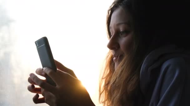 Hermosa chica caucásica utiliza un teléfono en un tren sobre un fondo de puesta de sol, 4k . — Vídeos de Stock