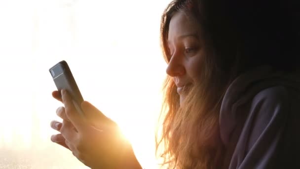 Belle fille caucasienne utilise un téléphone dans un train sur un fond de coucher de soleil et regarde par la fenêtre, 4k . — Video