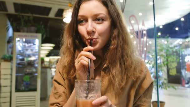 Menina bonita bebe smoothies de uma palha em um café — Vídeo de Stock