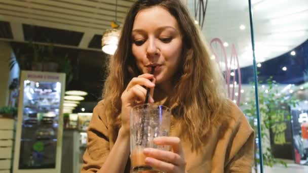 Hermosa chica propone beber batidos de una paja en un café — Vídeo de stock