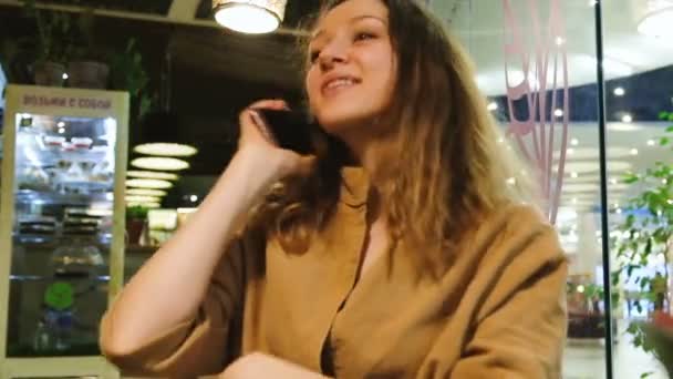 Hermosa chica responde a una llamada y habla por teléfono en un café — Vídeos de Stock