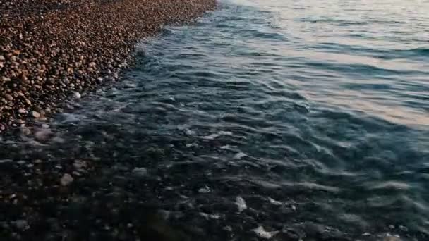 Olas azules en cámara lenta en una playa de guijarros al atardecer de cerca — Vídeos de Stock