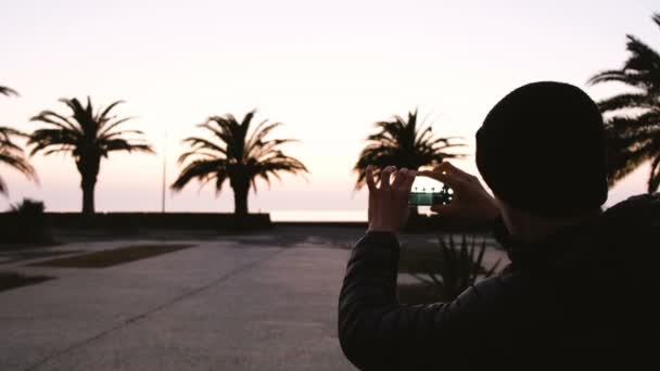 Un homme prend des photos de palmiers sur le front de mer au coucher du soleil — Video