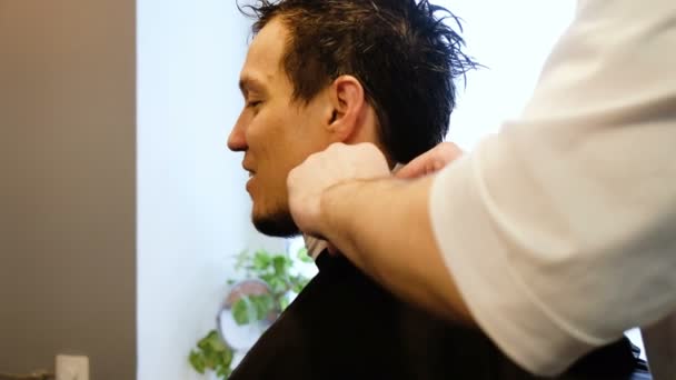Frisören lägger på ett skyddande cape förkläde till en man i en skönhetssalong — Stockvideo