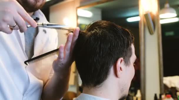 Парикмахер режет мужчину в парикмахерской — стоковое видео