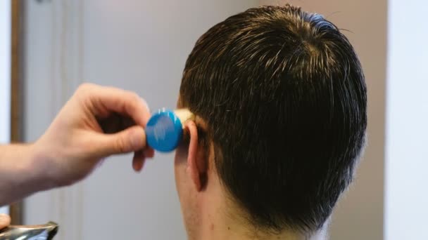 理发师把头发和一把电剃刀等同在理发店里的一个男人的耳朵后面。 — 图库视频影像