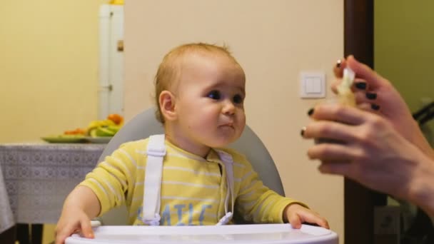 Mamá alimenta al bebé con comida del frasco, el bebé es travieso y no quiere comer — Vídeo de stock