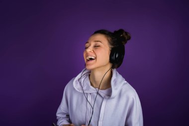 Güzel genç kız ile müzik ve bir kazak mor bir arka plan üzerinde kulaklık şarkı beyaz dişler