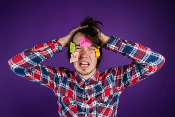 Man grabs his head, cries with his eyes closed and his mouth open, stickers on his face. A man is shocked by his obligations and routine - purple background