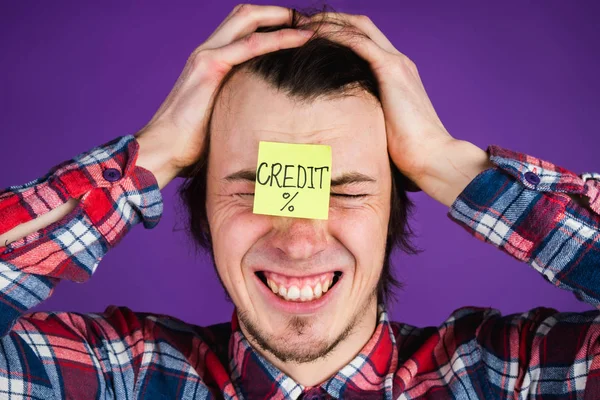 Caucasian man took a loan, grabs his head and cries, a close-up portrait. The man is shocked by the interest on the loan. Credit card sticker - purple background