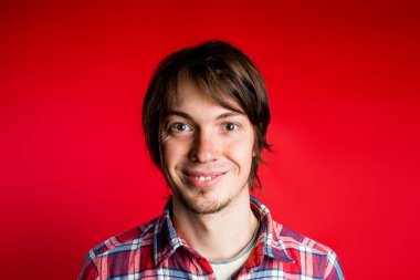 Hipster gülümsüyor ve kamera yakın çekim portre, kırmızı zemin üzerine ekose gömlekli bakar.