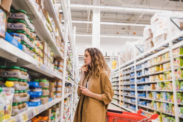 Сучасна молода жінка з планшетом вибирає дитяче харчування в супермаркеті — стокове фото