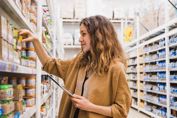 Молодая женщина с планшетом выбирает детское питание в супермаркете — стоковое фото