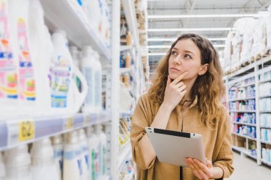 İş kadını ile bir tablet seçer ev Kimyasalları bir süpermarkette alışveriş hakkında düşünme