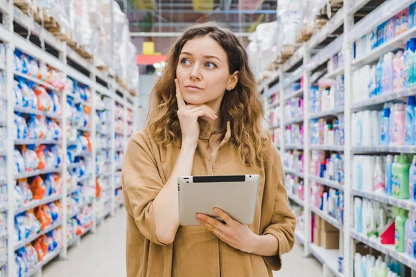 Jovem mulher de negócios está pensando em fazer compras com um tablet na mão em um supermercado — Fotografia de Stock