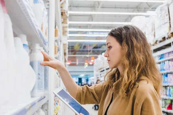 Jovem mulher de negócios escolhe química doméstica com um tablet em um supermercado — Fotografia de Stock