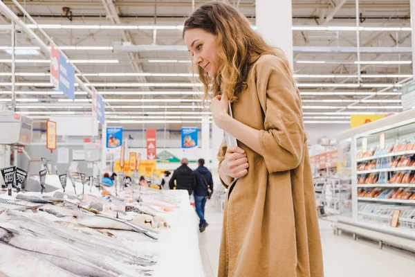 Nuori nainen, jolla on tabletti, poimii kalaa supermarketista — kuvapankkivalokuva