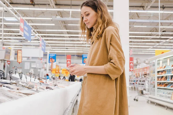 Молода ділова жінка з планшетом підбирає рибу в супермаркеті — стокове фото
