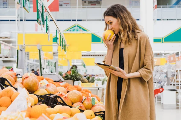 Mulher nova com uma pastilha cheira a toranja, escolhe comida em um supermercado — Fotografia de Stock