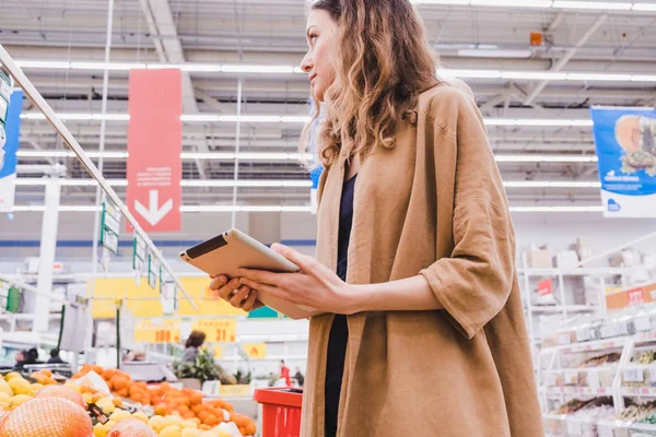 Молода ділова жінка з планшетом в руках купує їжу в супермаркеті — стокове фото
